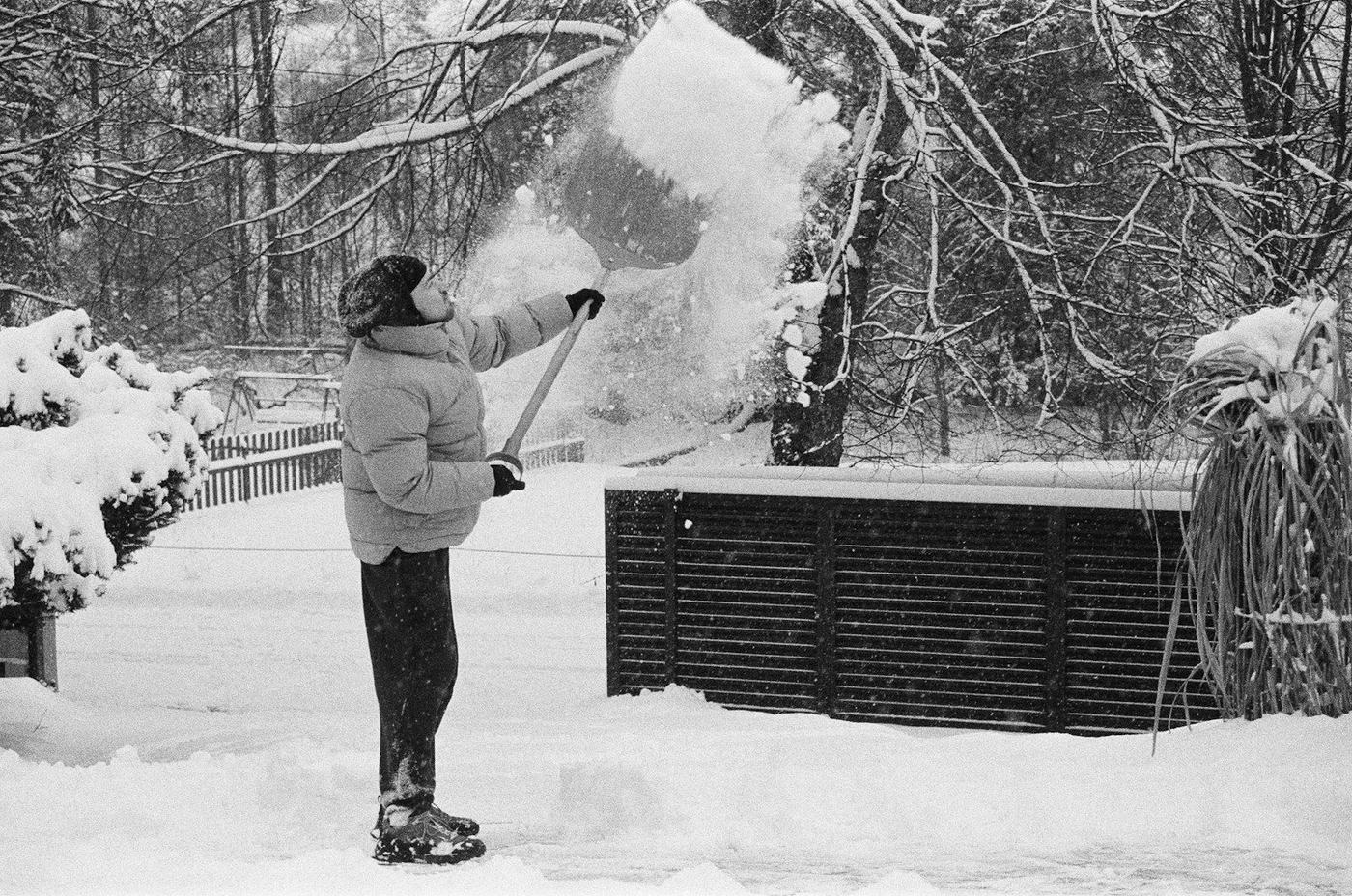 Person beim Schneeschaufeln vor einem verschneiten Garten